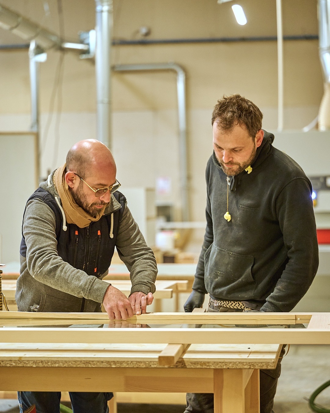 Deux hommes travaillent ensemble sur une pièce de bois dans un atelier de menuiserie.