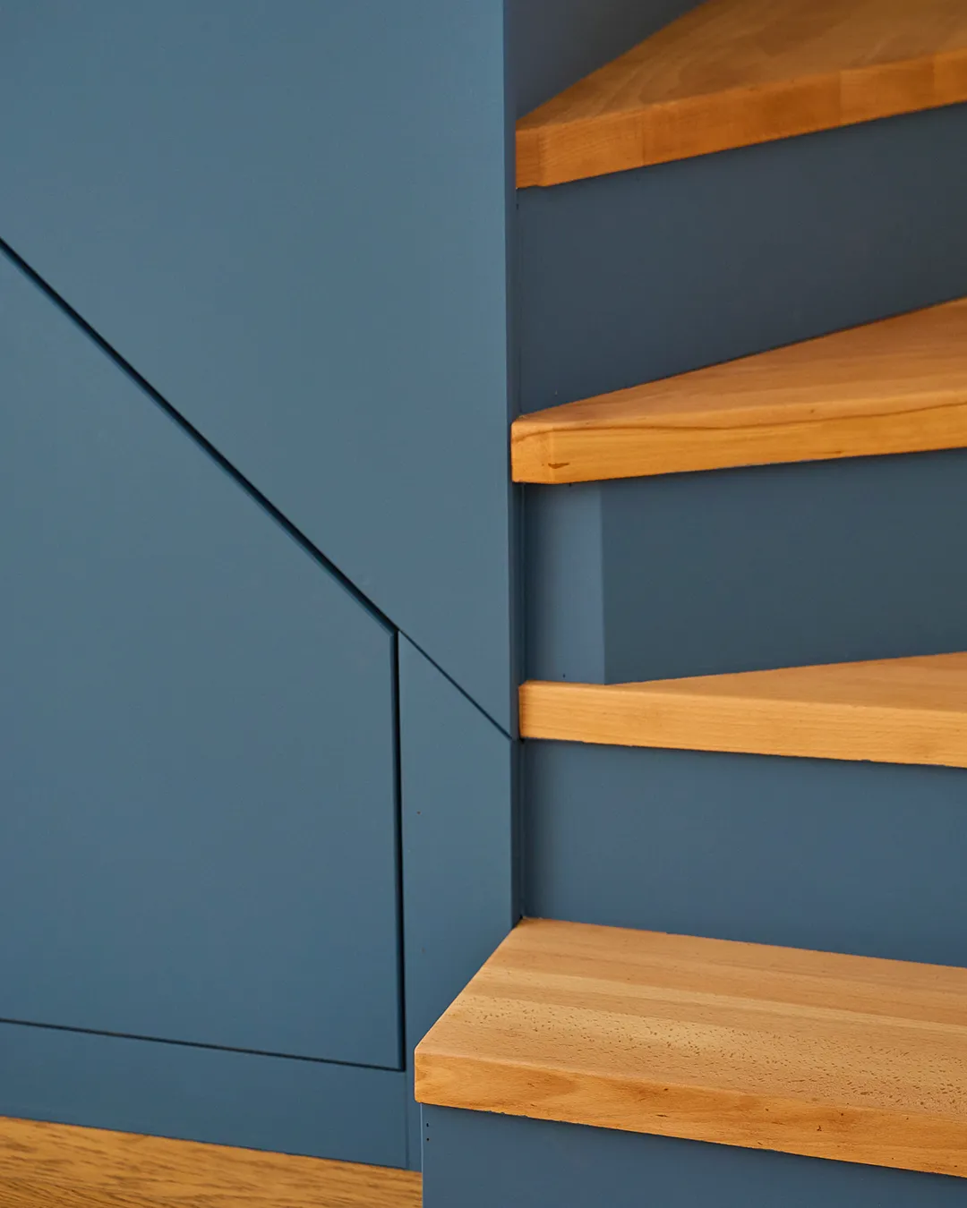 Escalier en bois clair avec contremarches peintes en bleu, détail d'un angle et d'un placard intégré.